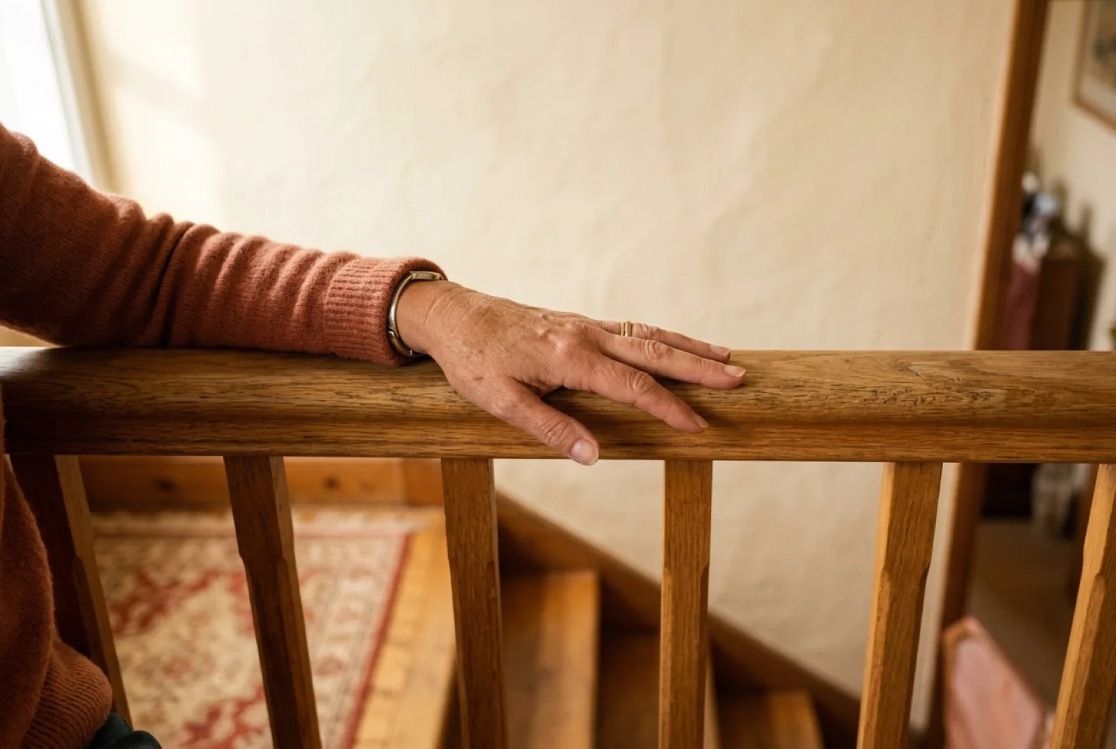 Une main posée sur la rampe en bois d'un escalier, dans une maison